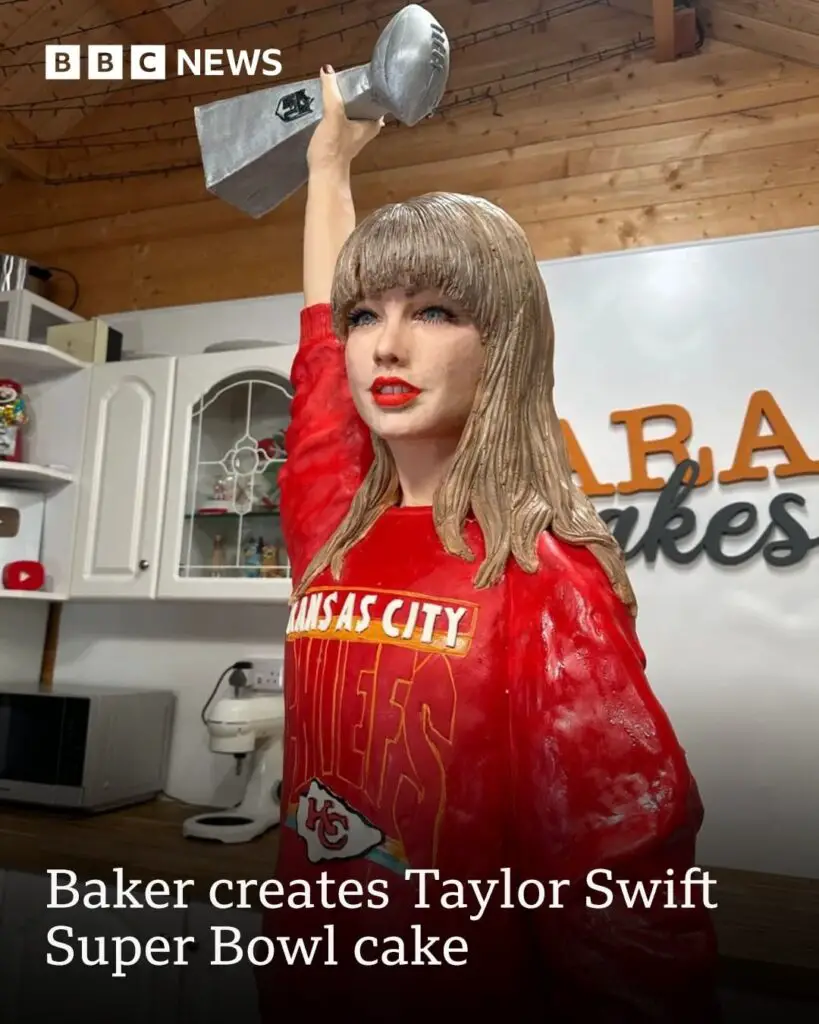 cake version of Taylor Swift is wearing a Kansas City Chiefs sweater and holding a Super Bowl trophy